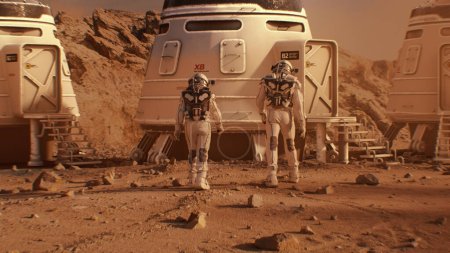 Foto de Dos astronautas en trajes espaciales caminan hacia la estación de investigación, colonia o base científica en Marte. Tripulado explorando la misión espacial en el planeta rojo. Concepto de colonización futurista y exploración espacial. - Imagen libre de derechos