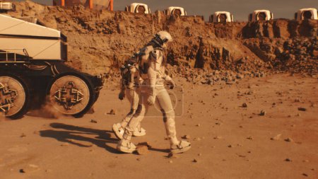 Foto de Dos astronautas en trajes espaciales caminan hacia la estación de investigación, colonia o base científica en Marte. Paseos en el rover impulsados por IA en el fondo. Misión espacial. Concepto de colonización y exploración futurista. - Imagen libre de derechos