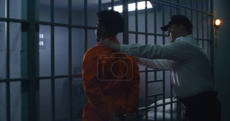 Foto de El empleado de la prisión le pone esposas a un preso culpable con uniforme naranja y lo saca de la celda. Los reclusos cumplen penas de prisión por delitos en prisión, centro de detención o correccional. - Imagen libre de derechos