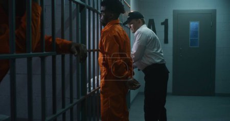 Foto de El alcaide trae a un nuevo prisionero a la cárcel y le quita las esposas. Los delincuentes afroamericanos cumplen condena de prisión en centros penitenciarios o centros de detención. Asesinos culpables en celdas de prisión. - Imagen libre de derechos