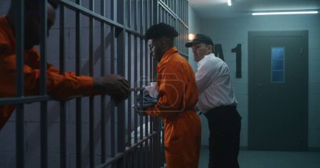 Foto de El alcaide trae a un nuevo prisionero a la cárcel y le quita las esposas. Los delincuentes afroamericanos cumplen condena de prisión en centros penitenciarios o centros de detención. Asesinos culpables en celdas de prisión. - Imagen libre de derechos