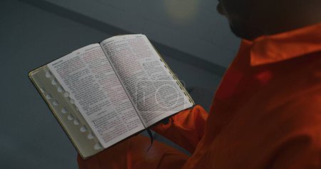 Téléchargez les photos : Gros plan sur la Bible. Un prisonnier afro-américain tient un livre à la main, lit, feuillette des pages. Homme criminel, délinquant purge une peine d'emprisonnement pour crime en cellule. Prison ou centre de détention. - en image libre de droit