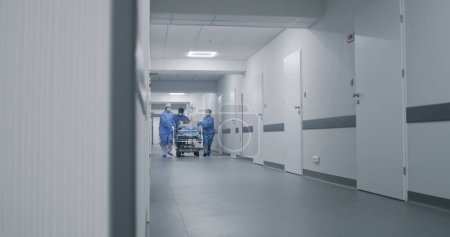 Ärzte, Krankenschwestern und Sanitäter laufen und schieben Tragen mit schwer verletzten Patienten in den Operationssaal. Medizinisches Personal rettet in der Notaufnahme Menschenleben. Korridor medizinischer Einrichtungen. Zeitlupe.