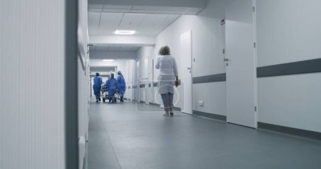 Ärzte, Krankenschwestern und Sanitäter laufen und schieben Bahren mit schwer verletzten Patienten in den Operationssaal. Medizinisches Personal rettet in der Notaufnahme Menschenleben. Flur der medizinischen Einrichtung. Zeitlupe.