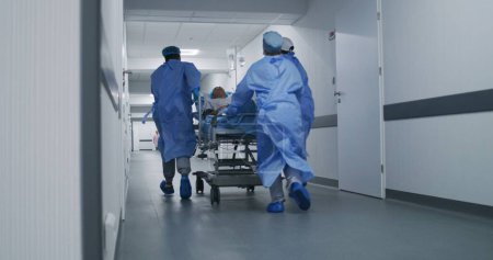 Ärzte, Krankenschwestern und Sanitäter laufen und schieben Bahren mit schwer verletzten Patienten in den Operationssaal. Medizinisches Personal rettet in der Notaufnahme Menschenleben. Flur der medizinischen Einrichtung. Zeitlupe.