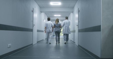 Photo for Following shot of doctors walking along the modern medical center corridor. Healthcare specialists and nurse enter the hospital room to patient or office. Medical staff in clinic hallway. - Royalty Free Image