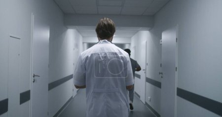 Téléchargez les photos : Spécialiste des soins de santé en uniforme blanc marche couloir du centre médical. Le docteur prend rendez-vous avec les patients. Personnel médical au travail dans le couloir de la clinique. - en image libre de droit