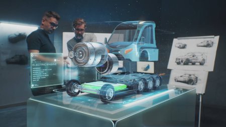 Téléchargez les photos : Deux ingénieurs automobiles masculins développent un nouveau camion écologique avec moteur électrique à l'aide d'un ordinateur tablette et d'un hologramme de réalité augmentée. Graphiques 3D de véhicule high-tech en développement. Animation VFX. - en image libre de droit