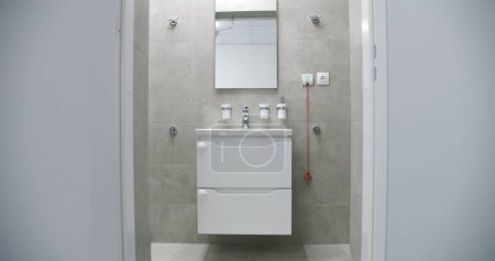 Photo for Dolly shot of white sink with mirror above it in bright and well-equipped bathroom with modern design in comfortable hospital ward. Sink, toilet and shower in medical facility or clinic. Zoom in. - Royalty Free Image