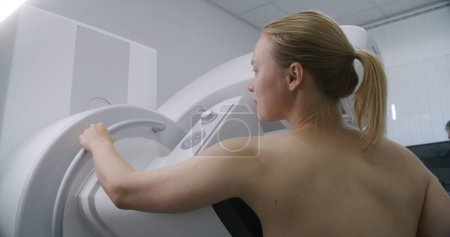 Photo for Caucasian adult woman stands topless in hospital radiology room. Female patient undergoing mammography screening procedure using mammogram machine. Breast cancer prevention. Modern clinic equipment. - Royalty Free Image