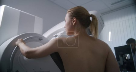 Foto de Mujer adulta en topless sometida a un chequeo de exploración mamográfica en la sala de radiología clínica. El médico masculino instala una máquina de mamografía con computadora. Prevención del cáncer de mama. Moderno hospital brillante. - Imagen libre de derechos