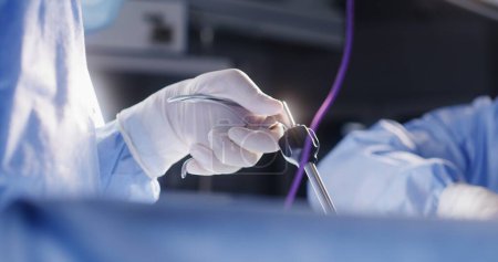 Primer plano de manos de cirujanos profesionales que realizan operaciones con herramientas laparoscópicas. El personal médico en conjunto salva al paciente gravemente lesionado en la sala de cirugía. Médicos trabajan en instalaciones médicas modernas.