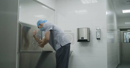 Photo for Professional surgeon in uniform washes hands before surgical operation. Paramedic prepares to performing surgery with seriously injured patient. Personnel work in modern medical facility. Slow motion. - Royalty Free Image