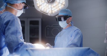 Photo for Team of surgeons in protective glasses use laparoscopic tools during surgery. Doctors and paramedics perform surgical operation with seriously injured patient. Medical staff work in modern hospital. - Royalty Free Image