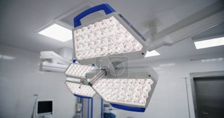 Téléchargez les photos : Dolly shot de lampe de fonctionnement LED suspendue au plafond dans la salle de chirurgie de l'hôpital moderne avec un équipement avancé prêt à l'emploi. Bloc opératoire lumineux dans une clinique ou un établissement médical. - en image libre de droit