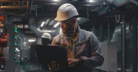 Photo for Multiethnic team of factory specialists work on modern factory using laptop and tablet computers. Heavy industry workers wearing safety uniform and hard hat check pipes. Industrial energy facility. - Royalty Free Image