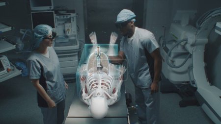 Foto de Diversos cirujanos en auriculares AR trabajan en quirófano usando la exhibición holográfica futurista. Gráficos 3D de esqueleto humano virtual y órganos. Tecnología de cirugía asistida por IA. Medicina de alta tecnología. - Imagen libre de derechos