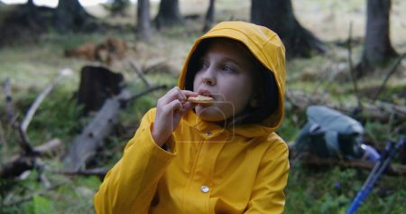 Photo for Tourist girl sits in beautiful forest and eats snacks. Young hiker rests in camp after long walking trek in the mountains. Concept of tourism and outdoor exploration. Outdoor activities. Slow motion. - Royalty Free Image