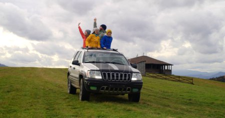 Photo for Group of tourists together ride on vacation in mountains. Hikers standing up through sunroof of car dance and wave hands on road trip. People enjoy drive in car hatch. Outdoor recreation. Slow motion. - Royalty Free Image