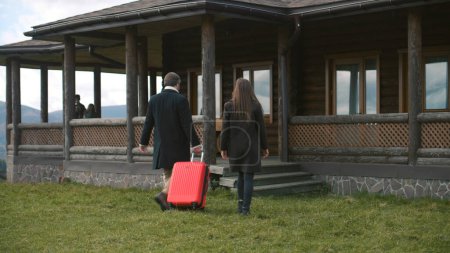Photo for Couple with kids walks to wooden cottage with suitcase. Happy family with children settles in rented modern house in countryside for holidays or moves into new home property. Real estate. - Royalty Free Image