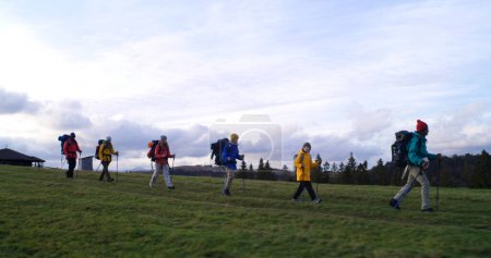 Photo for Full shot of diverse group of tourists walking on trail after sleepover in big house. Hiking buddies during trip or trek to mountains on their vacation in autumn. Tourism and active leisure concept. - Royalty Free Image