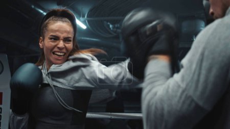 Photo for Close up of female fighter in boxing gloves practicing fighting technique and exercising before match in gym. Athletic boxer hits punching mitts on boxing ring. Physical activity and workout concept. - Royalty Free Image