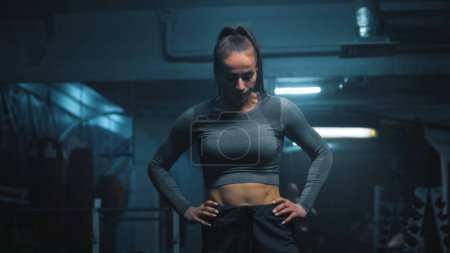 Photo for Strong woman with athletic body wearing sportswear lifts and does vigorous exercises with empty barbell in dark gym with LED lighting. Female athlete trains before sport competition. CrossFit workout. - Royalty Free Image