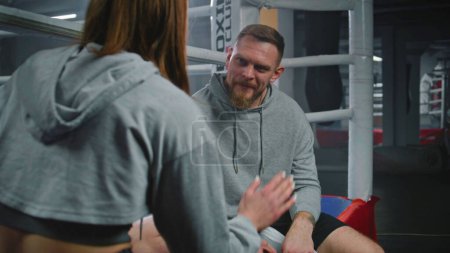 Photo for Female boxer sits on ring and talks with male trainer about fight. Coach consults boxer and explains fighting technique. Woman prepares to fighting competition in gym. Physical activity and workout. - Royalty Free Image