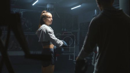 Photo for Athletic fighter in boxing gloves trains and exercises for fighting championship. Woman hits punching mitts and practices in fighting techniques with adult trainer. Physical activity and workout. - Royalty Free Image
