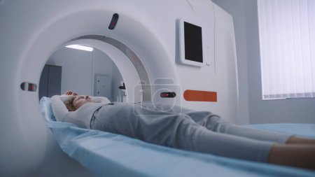 Téléchargez les photos : Plan rapproché de la femme allongée sur un lit scanner CT ou PET ou IRM et se déplaçant à l'intérieur de la machine. Balayage du corps et du cerveau des patients à l'aide d'équipements modernes de haute technologie. Installation médicale avec des technologies de pointe. - en image libre de droit
