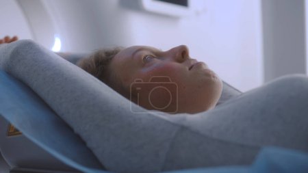 Foto de Primer plano de retrato de una mujer acostada en una tomografía computarizada o PET o resonancia magnética escaneada y moviéndose dentro de la máquina. Escaneando al paciente con tecnologías médicas avanzadas. Laboratorio médico con equipos modernos de alta tecnología. - Imagen libre de derechos