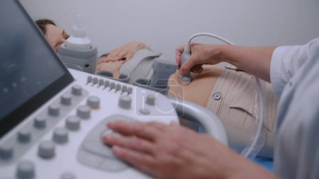 Téléchargez les photos : Médecin utilisant une machine d'échographie avec moniteur numérique. Médecin spécialiste effectue un diagnostic par ultrasons à la patiente enceinte. Clinique moderne avec équipement avancé. Concept de soins de santé. Gros plan. - en image libre de droit