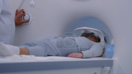 Photo for Female patient lies down on MRI or CT scan bed moving inside the machine for scanning brain and body. Radiologist controls and turns on scanner for cancer prevention examination for Caucasian woman. - Royalty Free Image