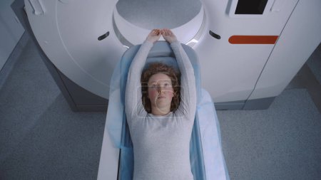 Foto de Inyección de cerca de una paciente hembra acostada en una tomografía computarizada, una PET o una resonancia magnética que se mueve dentro de la máquina. El equipo de alta tecnología escanea el cuerpo y el cerebro del paciente en un centro médico con tecnologías de vanguardia. - Imagen libre de derechos