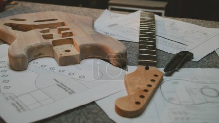 Photo for Wooden blank of guitar body, guitar neck, drawings and tools for manufacturing lie on the table. Working day in modern workshop for musical instruments making. Handmade and entrepreneurship concept. - Royalty Free Image