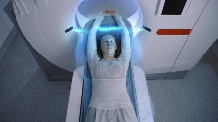 Female patient undergoes MRI or CT scan, lies on bed moving inside machine. Visual effects of scanning brain and body of woman. High-tech augmented reality and futuristic equipment in advanced clinic.