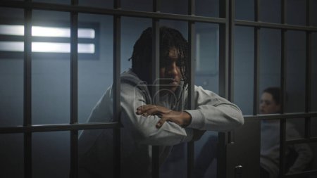 Foto de Adolescente afroamericano deprimido con tatuajes está en la celda de la cárcel y mira a la cámara. Un joven recluso cumple condena de prisión por delito. Centro de detención juvenil o correccional. - Imagen libre de derechos