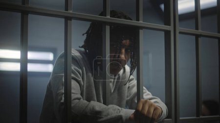 Foto de Adolescente afroamericano deprimido con tatuajes está en la celda de la cárcel y mira a la cámara. Un joven recluso cumple condena de prisión por delito. Centro de detención juvenil o correccional. - Imagen libre de derechos