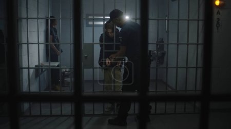 Warden brings young prisoner in jail cell and takes off his handcuffs. Multi ethnic teenagers serve imprisonment term in correctional facility or detention center. Guilty inmates in prison cells.