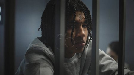 Photo for Angry African American teenage prisoner with face tattoos stands in prison cell in jail and looks at camera. Young criminal serves imprisonment term for crime. Juvenile detention center. Portrait. - Royalty Free Image