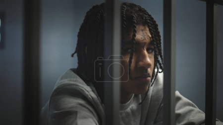 Téléchargez les photos : Un adolescent afro-américain en colère tatoué au visage se tient dans une cellule de prison et regarde une caméra. Un jeune criminel purge une peine d'emprisonnement pour crime. Centre de détention pour mineurs. Portrait. - en image libre de droit