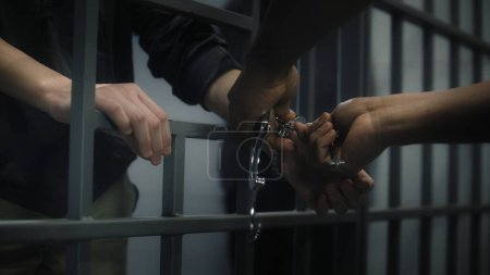 Wärter legt jungen Gefangenen Handschellen an. Multiethnische Teenager verbüßen ihre Haftstrafe in einer Justizvollzugsanstalt oder in einem Internierungslager. Junge Häftlinge in der Gefängniszelle. Justizsystem. Nahaufnahme.