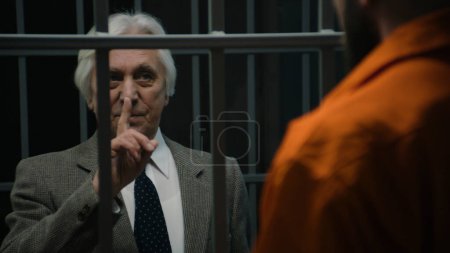 Anwalt spricht mit Verbrecher in orangefarbener Uniform, der in Gefängniszelle steht und seine Dienste anbietet. Häftling verbüßt Haftstrafe für Verbrechen in Justizvollzugsanstalt Häftling in der Haftanstalt oder im Gefängnis.