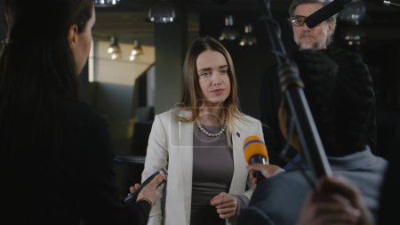 Positive female politician or consul of the European Union answers journalists questions and gives interview for media and television news in government building. Political speech at press conference.