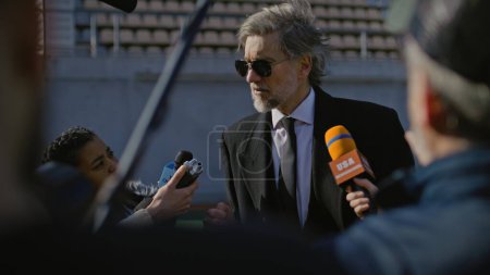 Photo for Successful private investor at press conference for TV news. Organization representative answering press questions and giving interview outside a soccer stadium. Journalists crowd on press campaign. - Royalty Free Image