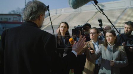 Photo for Interview of private investor at press conference near soccer field for TV news. SEO or director of football team answering press questions and giving interview to journalist crowd. Press conference. - Royalty Free Image