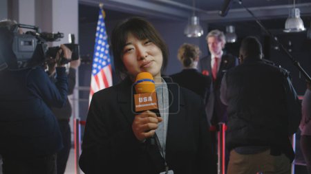 Photo for Asian anchorwoman reports breaking news live from government building. Female journalist leads broadcast for political television program from press conference with American politician or US President - Royalty Free Image