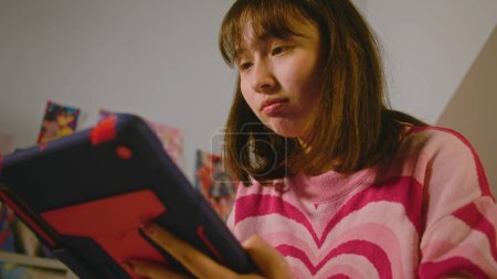 Photo for Teen girl chats or scrolls social networks using digital tablet computer while sitting in the cozy bedroom. Mongolian girl spending leisure time or weekend and having fun at home. Lifestyle concept. - Royalty Free Image