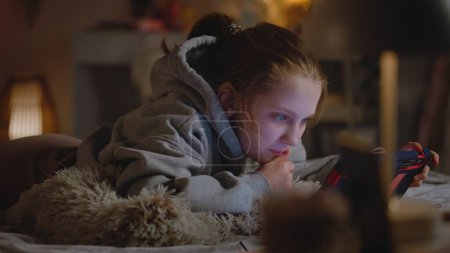Photo for Young girl lies on bed at home, surfs the Internet or scrolls social networks using tablet computer. Caucasian teenager spends leisure time in cozy and comfort bedroom in daytime. Lifestyle concept. - Royalty Free Image