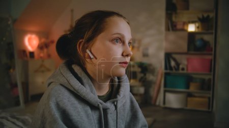 Photo for Young beautiful girl in wireless headphones sits on the bed in cozy and comfort bedroom and listens to music. Caucasian teenager spends leisure time after school at home in daytime. Lifestyle concept. - Royalty Free Image